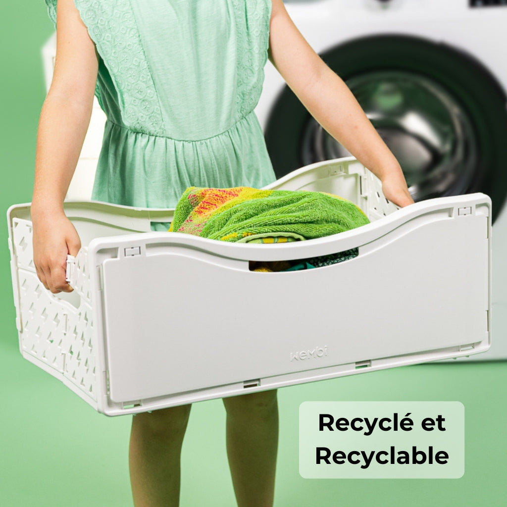 Panière magnétique à linge pliable, portée par une femme devant une machine à laver, conçue pour se ranger contre le tambour. MADE IN EU. Recyclée et recyclable. Wembi innovation. 